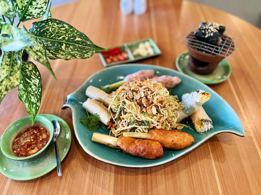 Vietnamese appetizer platter with grilled pork skewers, fried spring rolls, and fresh salad rolls served on a green leaf-shaped plate at Spice Viet Hue
