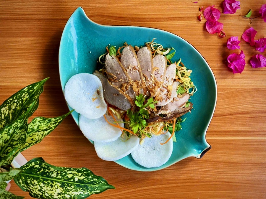 ietnamese pork salad with green papaya, crispy shallots, and rice crackers beautifully presented on a leaf-shaped plate at Spice Viet Hue