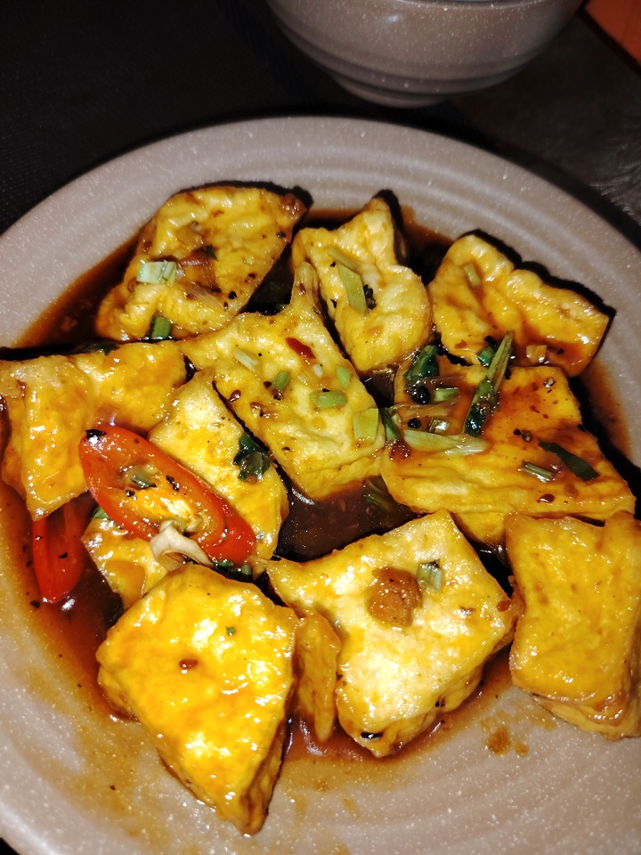 Golden-fried tofu simmered in savory tomato sauce, garnished with green onions and ground pepper, a flavorful vegetarian dish.