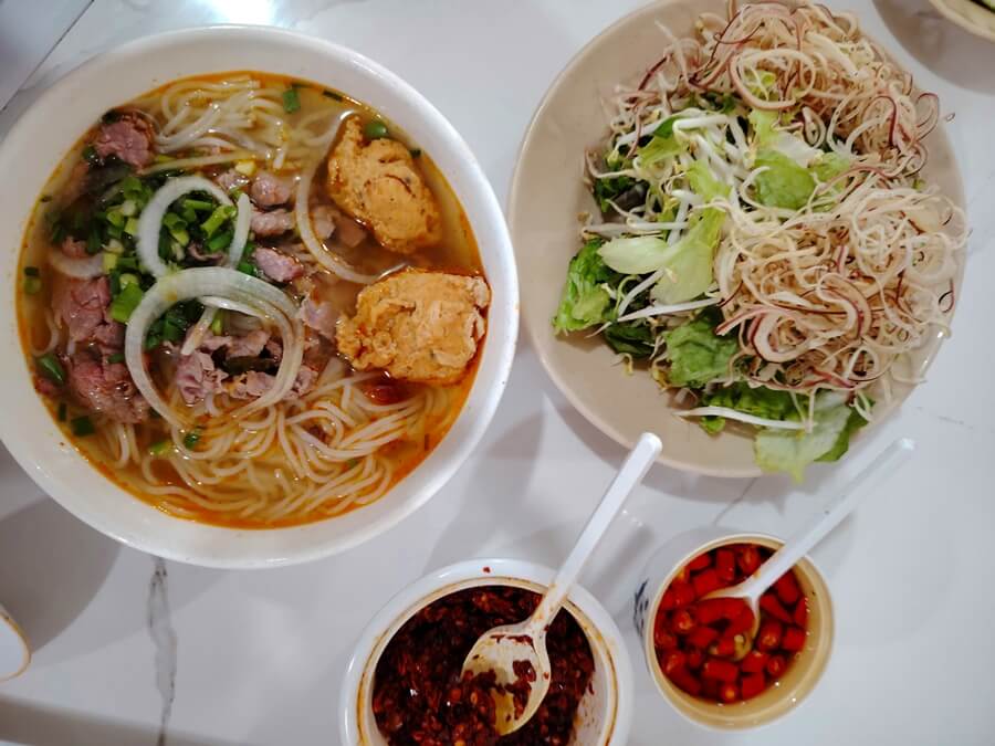 Bun Bo Hue served with banana flowers, herbs, bean sprouts, chili sauce, and fish sauce
